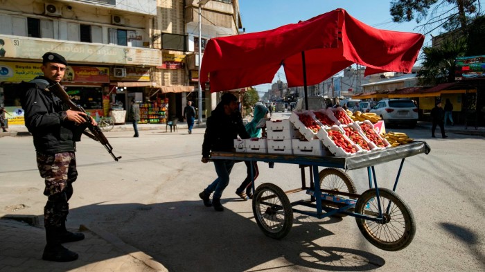 Members of Syrian Kurdish security forces patrol a street, as stallholders push their market cart of fruit and vegetables in the Kurdish-majority city of Qamishli in northeastern Syria on February 26 2025